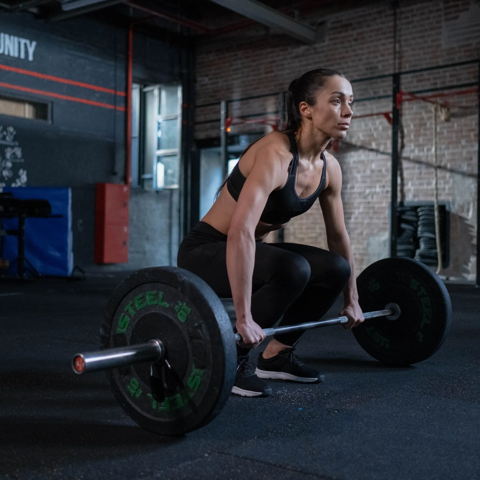 A determined woman prepares to lift barbell in a gym, showcasing strength and focus.