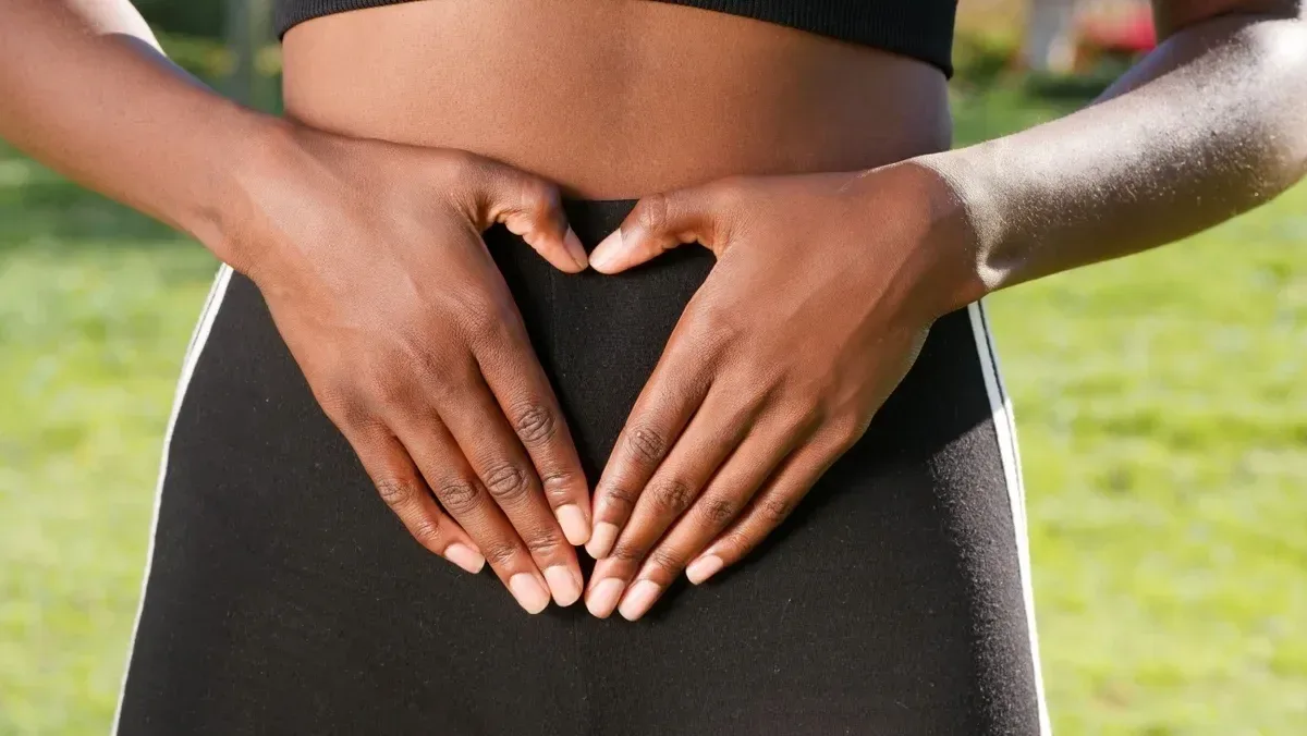 Close-up of hands forming a heart shape on woman's belly